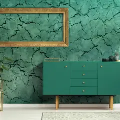 Parete con finitura in stucco materico verde intenso, incorniciata da un elegante mobile verde e piante in vasi dorati.