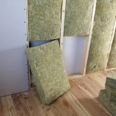 Installazione di isolamento interno pareti con pannelli di lana di roccia in una stanza con pareti in cartongesso e pavimento in legno.
