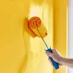 Mano che dipinge un muro di giallo brillante con un rullo. La vernice ha un bellissimo colore opaco che copre uniformemente la superficie.