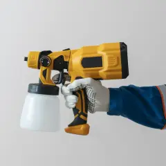 Mano guantata impugna una pistola per verniciatura a spruzzo gialla e nera, pronta per un lavoro di finitura impeccabile.