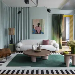 Salotto con divano bianco bouclé, poltrona in pelle, tappeto geometrico e lampada da terra, in un audace stile massimalista.