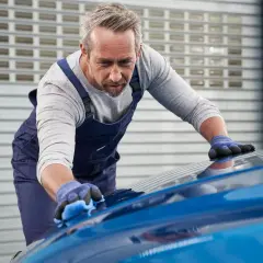 Un esperto opera la verniciatura auto con cura, lucidando la carrozzeria blu brillante.