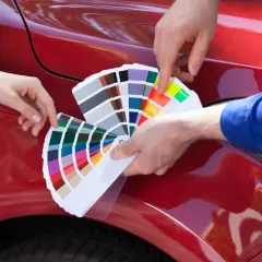 Scelta colore per la verniciatura auto. Due mani tengono un campionario di colori su un'auto rossa lucida.