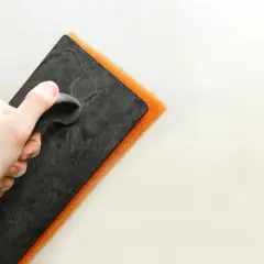 Mano che impugna una spatola con spugna arancione per la pittura tamponato.