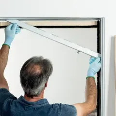 Uomo con guanti blu installa la guida per una porta scorrevole fai da te.