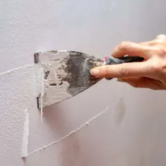 Mano usa una spatola per rimuovere la pittura vecchia da un muro.