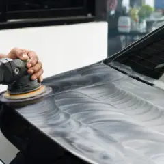 Mani esperte lucidano la lucida carrozzeria auto con una lucidatrice, creando un effetto specchiato.