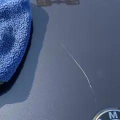 Un panno blu accanto a un graffio sulla vernice dell'auto, pronto per imparare come ritoccare vernice auto.
