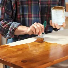 Mano che applica mordente su legno con pennello. Il mordente significato è dare colore e profondità al legno.