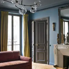 Soggiorno elegante con pareti blu balena Pantone, divano bordeaux, tendaggi ocra e camino in marmo.