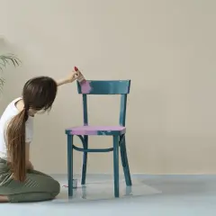 Donna inginoxida una sedia blu con vernice lucida, applicando un colore rosa pastello per opacizzare la finitura.