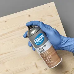 Mano con guanto blu tiene bomboletta spray "Ferox Primer Fondo per Legno", pronta per preparare la superficie.