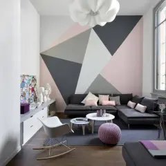 Soggiorno moderno con parete decorata con idee pittura geometrica in rosa, grigio e bianco. Divano angolare, tavolini e sedie di design.