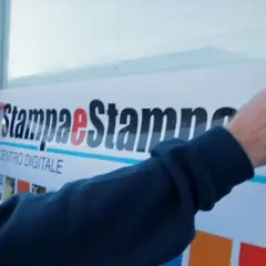 Mani applicano un grande adesivo con logo "Stampa e Stampe Centro Digitale" su una superficie, mostrando come applicare un adesivo senza bolle per un risultato perfetto.