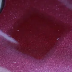 Superficie metallizzata color bordeaux con riflessi scintillanti. Il trasparente è un colore che cattura la luce, creando un effetto quasi liquido.