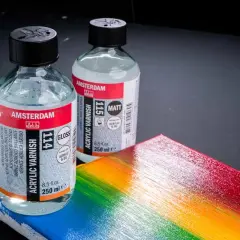 Due flaconi di vernice acrilica Amsterdam, uno lucido e uno opaco, accanto a una tavolozza arcobaleno. Ricorda che la vernice acrilica è tossica.