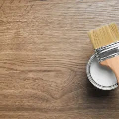 Pennello e barattolo di vernice bianca su fondo in legno, pronti per iniziare a come verniciare un mobile in legno.