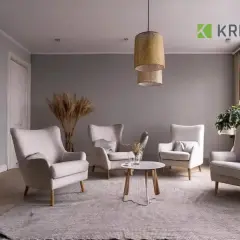 Salotto accogliente con poltrone color ecru, tappeto grigio e un tavolino centrale. Pareti grigie e tende color tortora completano l'arredo.