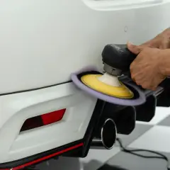 Dettaglio di un professionista che lucida il paraurti di un'auto bianca con una lucidatrice orbitale, mostrando la cura nel verniciare paraurti senza smontarlo.