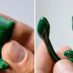 Due figurine verdi di gatto, stampate in 3D, tenute tra le dita. I colori per stampe 3d brillano sotto la luce.