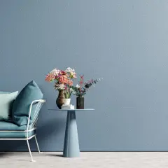 Divano blu petrolio con cuscini, tavolino azzurro con vasi di fiori. La materia e i colori creano un'atmosfera rilassante.