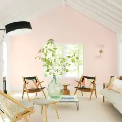 Salotto luminoso con pareti color aragosta tenue, mobili in legno chiaro, un divano beige e sedie con cuscini colorati.