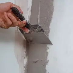 Mano con spatola applica materiale per chiudere i buchi nel muro senza stucco, riparando crepe e imperfezioni.