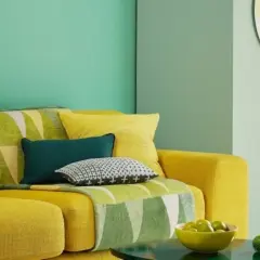 Divano giallo acceso con cuscini colorati e una coperta con motivi geometrici in **colore verde**. Sul tavolino, una ciotola di lime.