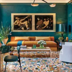 Soggiorno con divano arancione, quadri classici e pavimento a terrazzo. La differenza tra ottanio e petrolio è evidente nei toni del muro e delle tende.