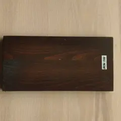 Tavola scura con evidenti venature del legno, su sfondo chiaro con venature simili. Etichetta bianca con scritta "NOCE MEDIO".