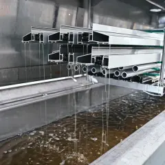 Profili in alluminio immersi in un bagno per la sverniciatura chimica, gocciolando liquido marrone.