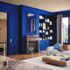Un soggiorno elegante con pareti blu intenso, camino in marmo, libreria e divano bianco. Un'altra stanza con tavolo e sedie è visibile attraverso un'apertura.