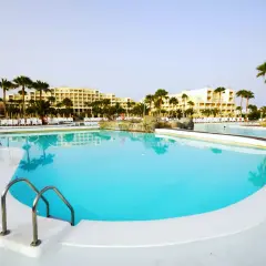 Piscina con acqua cristallina e palme, ideale per una vacanza rilassante. La **clorocaucciù scheda tecnica** descrive i materiali resistenti usati.