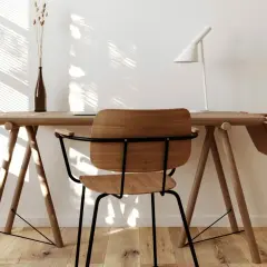Scrivania in legno chiaro con sedia, lampada bianca e vaso. Perfetti colori da abbinare al legno chiaro per un ambiente luminoso e naturale.