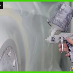 Mano che tiene una pistola a spruzzo per verniciare auto su vernice esistente, con la carrozzeria protetta da teli.