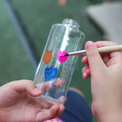 Bambino dipinge fiori su una bottiglia trasparente, un modo creativo per imparare come colorare la plastica trasparente.
