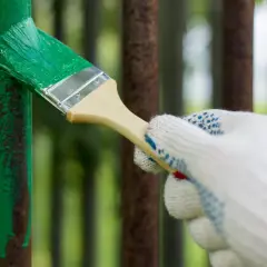 Mano guantata che inizia a verniciare un cancello in ferro con vernice verde brillante, coprendo la ruggine.