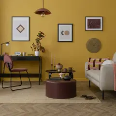 Un accogliente soggiorno con pareti color ocra, un divano beige, una scrivania nera e un tavolino rotondo.