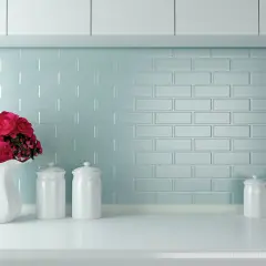 Un vaso bianco con fiori rossi e barattoli su un piano di lavoro. Un'idea per come verniciare le piastrelle della cucina con un tocco di colore.