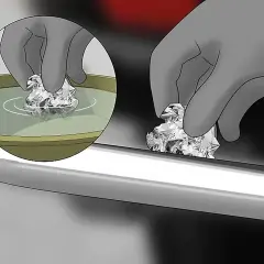 Mano con guanto pulisce con carta stagnola una cromatura rovinata, immergendola prima in un liquido.