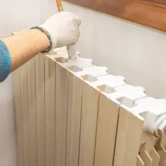 Mano con guanto bianco che dipinge un termosifone con pennello, un modo pratico per verniciare termosifoni senza smontarli.