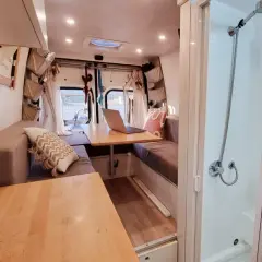 Interno camper con divanetti, tavolo e un box doccia in legno fai da te.