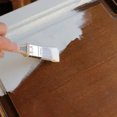 Mano che dipinge con pennello bianco su mobile in legno scuro. La cementite a cosa serve? A preparare la superficie per una finitura perfetta.