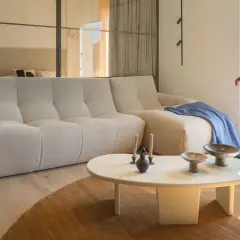Divano chiaro e tavolino bianco su un tappeto di colore marrone. Sul tavolino, vasi e candele. Sul divano, una coperta blu.