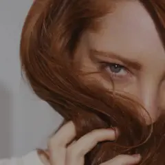 Occhi penetranti emergono da una cascata di capelli ramati, un invito a scoprire come fare il rosso scuro perfetto.