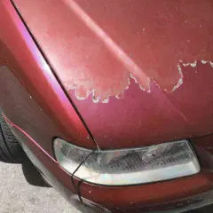 Vernice auto rovinata sul cofano rosso metallizzato, con scrostature evidenti che rivelano il primer.