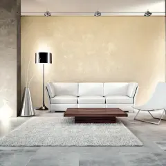 Soggiorno moderno con divano bianco, tavolino in legno scuro e un tappeto soffice. Le pareti presentano un effetto materico, quasi un effetto krokodil, che aggiunge profondità.