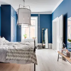 Camera da letto con accogliente parete azzurra, letto comodo, armadio blu e pavimento in legno chiaro.