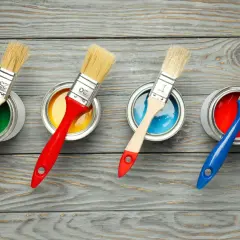 Quattro barattoli di vernice colorata (verde, giallo, blu, rosso) con pennelli pronti all'uso. La scelta della vernice giusta per il legno è fondamentale per un buon risultato.