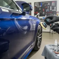 Un professionista usa una lucidatrice per riparare la carrozzeria di un'auto blu graffiata.